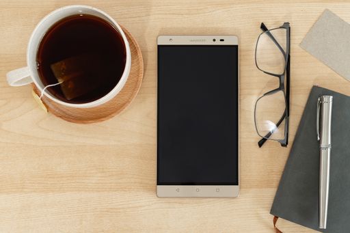A top view of a tablet, notebook, pen, and teacup on a wooden desk