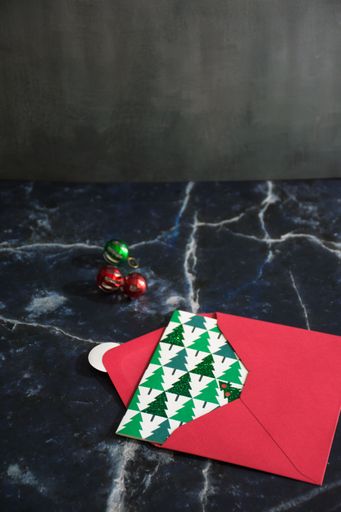 Festive Christmas card in red envelope on marble surface with ornaments, creating a holiday atmosphere.