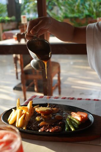 A hand pouring sauce on the dish with meat and vegetables