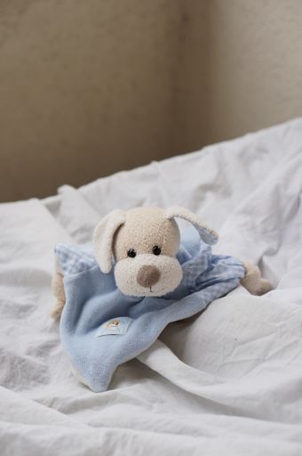 A vertical shot of a small soft plush dog on a bedsheet