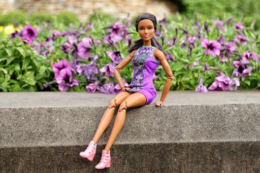 A closeup of a brunette dark-skinned Barbie doll sitting on a stone