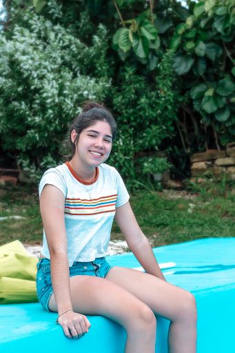 A vertical shot of a beautiful Hispanic girl sitting near the swimming pool in Cuba