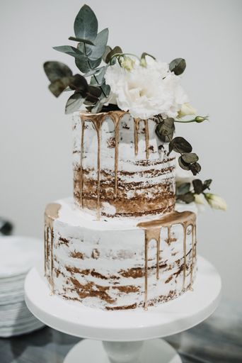 A vertical shot of a large white and gold wedding cake decorated with roses