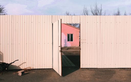 An open door of a white gate of a house under the sunlight and a cloudy sky in the countryside