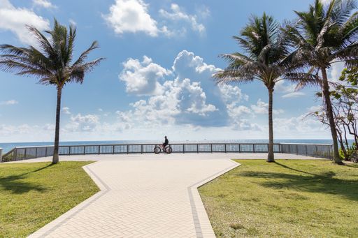 Landscape photograph of a man on a bicycle stopped by a railing while looking out over the Atlantic Ocean in Deerfield Beach, Florida.