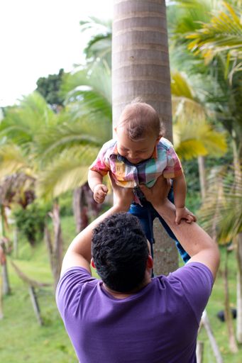 A young father playfully lifting his child in the air in the park