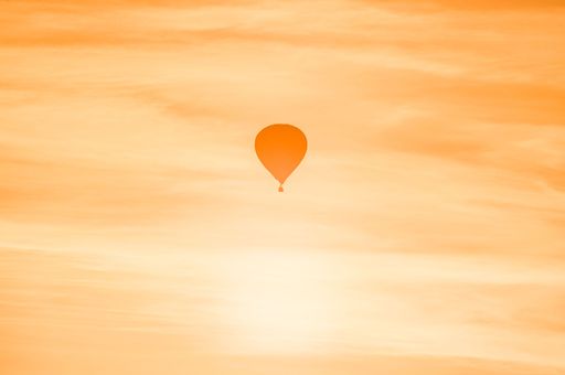 A solitary hot air balloon floats against a vibrant orange sky at sunset.