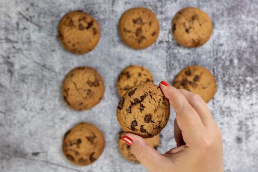 A top view of chocolate chip cookies on a textured surface with a woman holding one cookie