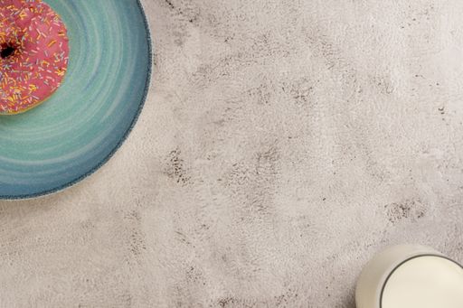 A top view of strawberry doughnut on a plate and a glass of milk on a concrete surface with space for your text