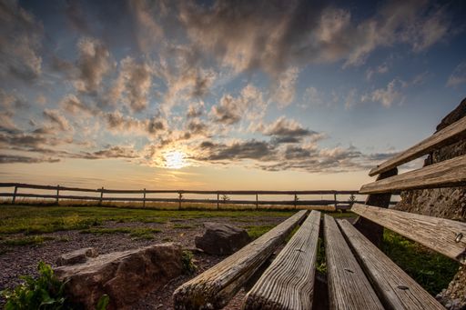 A wooden weathered old bench on the field gleaming under the sunrays in the cloudy sky
