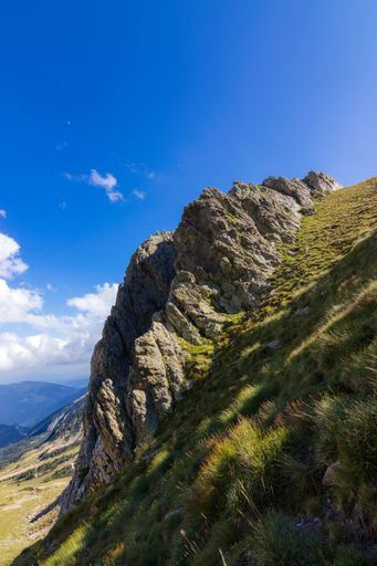 A beautiful view of the green rocky cliffs gleaming under the cloudy blue sky
