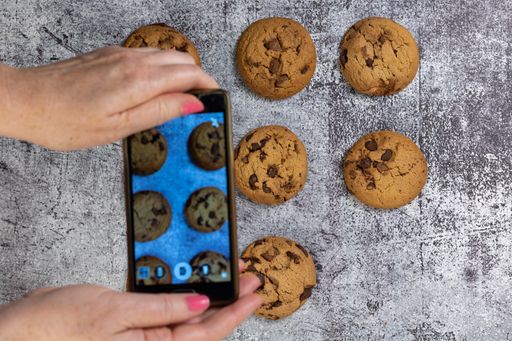 A woman taking a photo of chocolate chip cookies on a concrete table