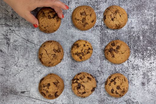 A top view of chocolate chip cookies on a textured surface with a woman taking one cookie