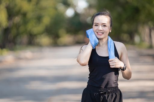 A healthy happy Asian runner in a black outfit jogging in a park during the sunset