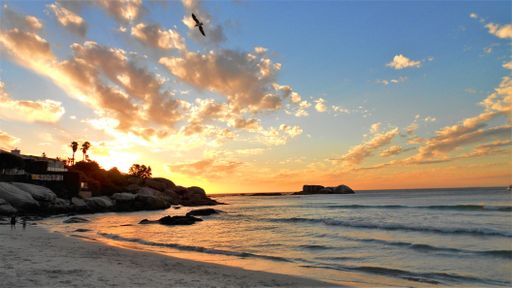 A beautiful shot of a beach shore near buildings under a blue and yellow sky at sunset in Clifton