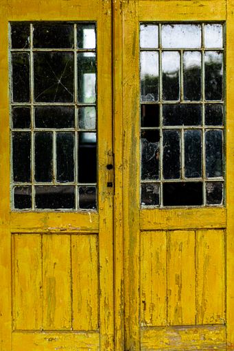 A vertical shot of an old wooden yellow door of an abandoned building