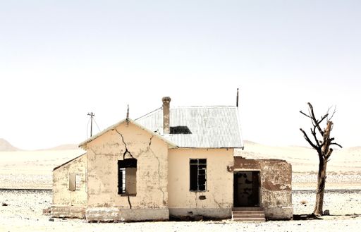 A beautiful shot of an old abandoned house in the middle of a desert near a leafless tree