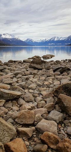 A vertical shot of a breakwater stones on the seaside and in front there are mountains covered with snow