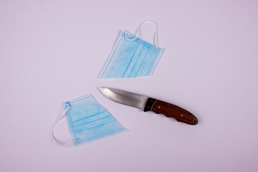 A top view of a sharp knife with a cut in half protective facemask on the white surface