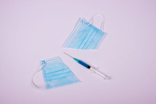 A top view of a cut protective facemask with a syringe filled with a drug on the white surface