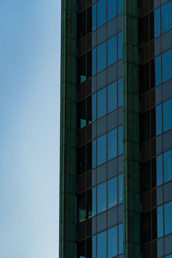 A close-up of a modern glass skyscraper facade against a clear blue sky, in Frankfurt