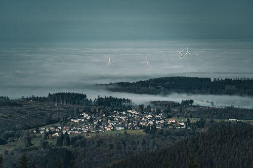 A majestic mountain rises above the clouds, shrouded in mist under a dark, moody sky.