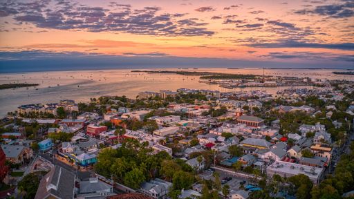 Aerial view of Key West at sunset, showcasing vibrant buildings, calm waters, and a colorful sky.