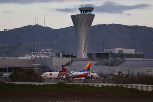 A Southwest Airlines Boeing 737-800 in the California One livery taxis toward its gate at SFO with the control tower and Sign Hill behind.