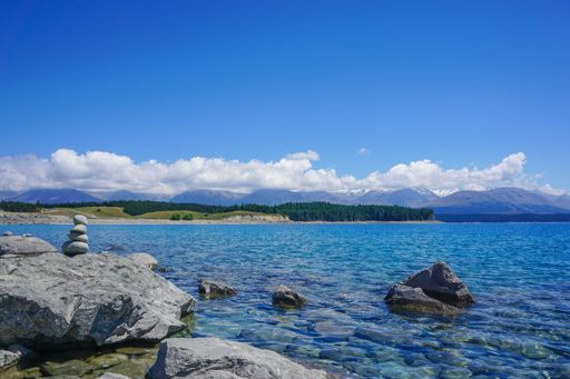 A view of Lake Tekapo with clear blue water and distant mountains under a blue sky in New Zealand.