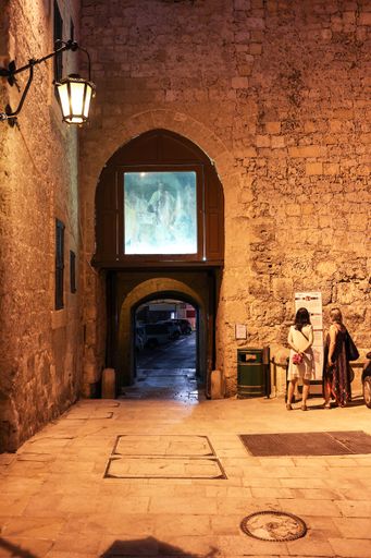 Medieval pointed arch of internal door of minor gate of Mdina, Malta, with painting of St. Paul in upper part. Two lady tourists reading info panels.