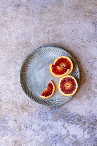 Peeled and sliced blood orange in ceramic plate on marble surface