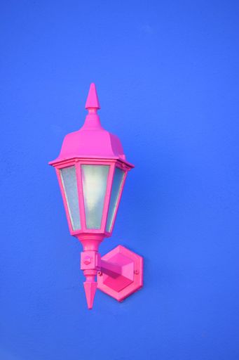A vertical shot of a pink sconce lamp attached to a blue wall