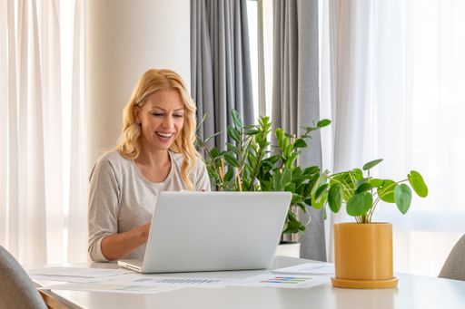 A Caucasian woman working remotely on a laptop and smiling