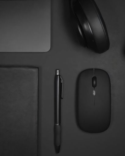 Flat lay of black office supplies including a laptop, headphones, pen, and mouse on a dark surface.