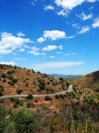 A vertical shot of a long trail through rocky dry mountains under a blue sky