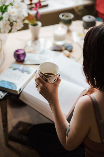 A vertical shot of a young female reading a book with a cup of coffee in hand