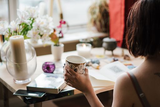 A selective focus shot of a young female reading a book with a cup of coffee in hand