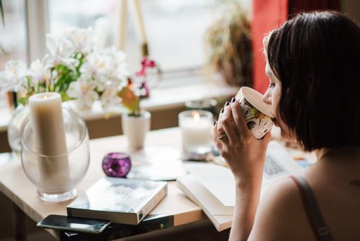 A selective focus shot of a young female drinking coffee with a book in front on the table