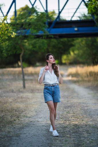 A young Spanish woman with headphones wearing shorts with a white shirt and walking in a park