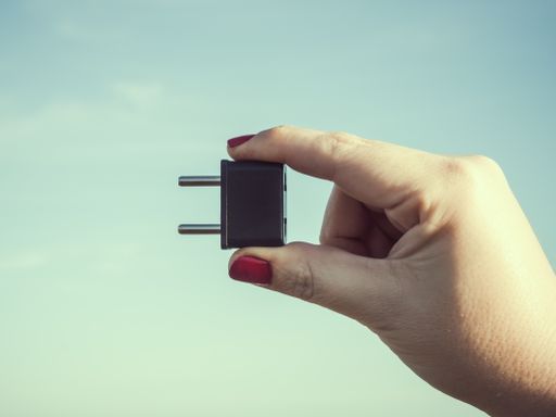 A closeup shot of a woman's hand holding a black plug isolated on a sky blue background