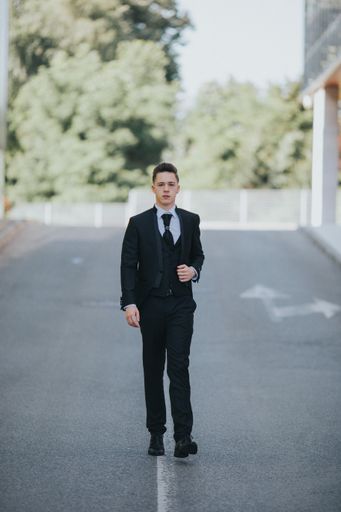 A young attractive Caucasian man with piercings wearing a black suit and walking in the street