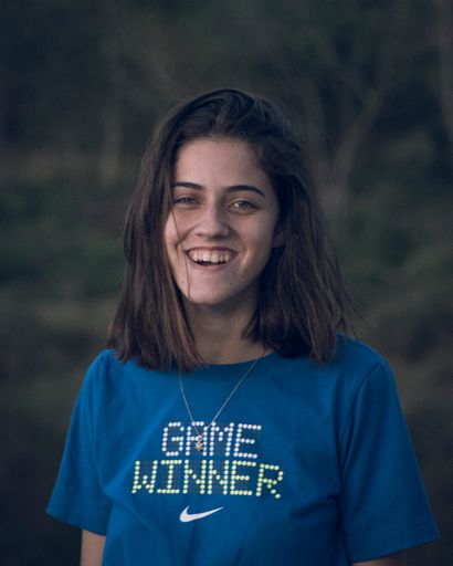 A vertical shot of a girl smiling wearing a blue t-shirt with the writing "Game winner" while looking at the camera