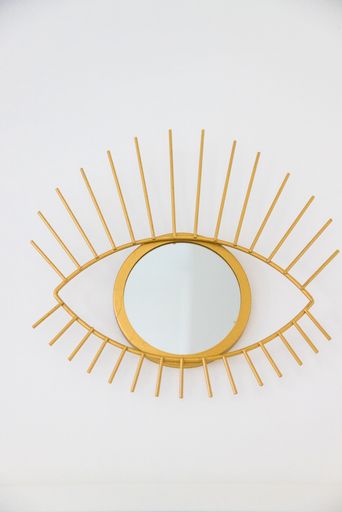 a vertical shot of a gold mirror shaped like an eye on a white wall