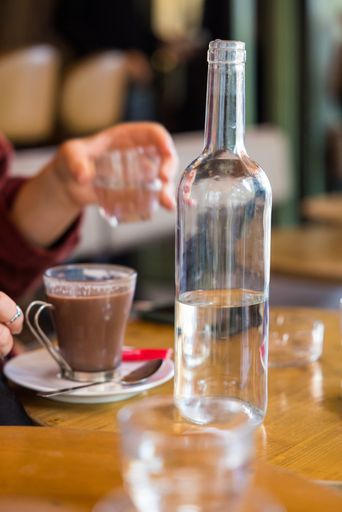A vertical shot of a glass bottle of water and coffee on a cafe table