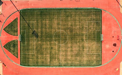 Aerial view of an empty soccer field with a surrounding running track, showcasing vibrant red and green colors.