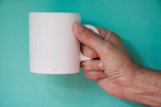 A hand holding a blank white mug on a green background