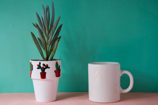 A blank white mug and a potted plant on green background with copy space
