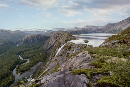A breathtaking view of a rocky mountain landscape with a serene lake and lush green forest under a clear sky.