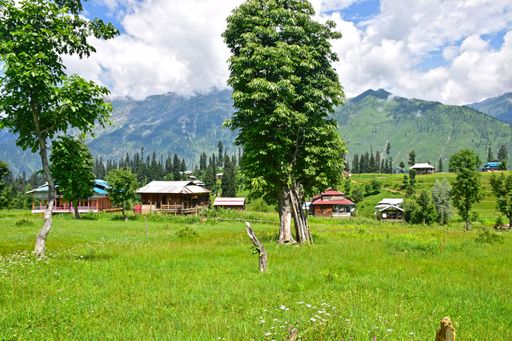 A mesmerizing green land with small houses and mountains in the background under a cloudy sky