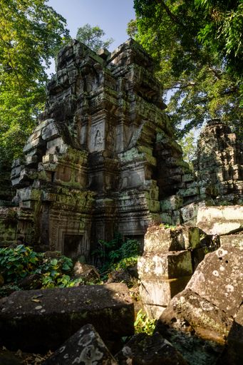 Ancient stone temple ruins surrounded by lush greenery in Angkor Wat, Cambodia, under a clear blue sky.
